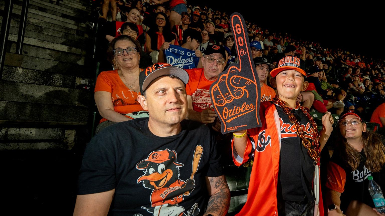 Father and son Orioles fans cheering in the stands, son holding an orange foam finger